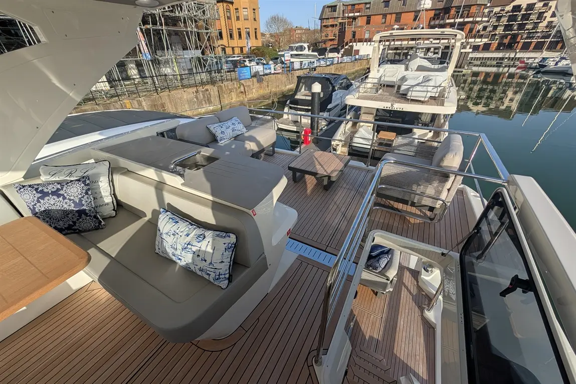Luxury boat deck with stylish seating, nautical cushions, a small table, and marina views in bright daylight.